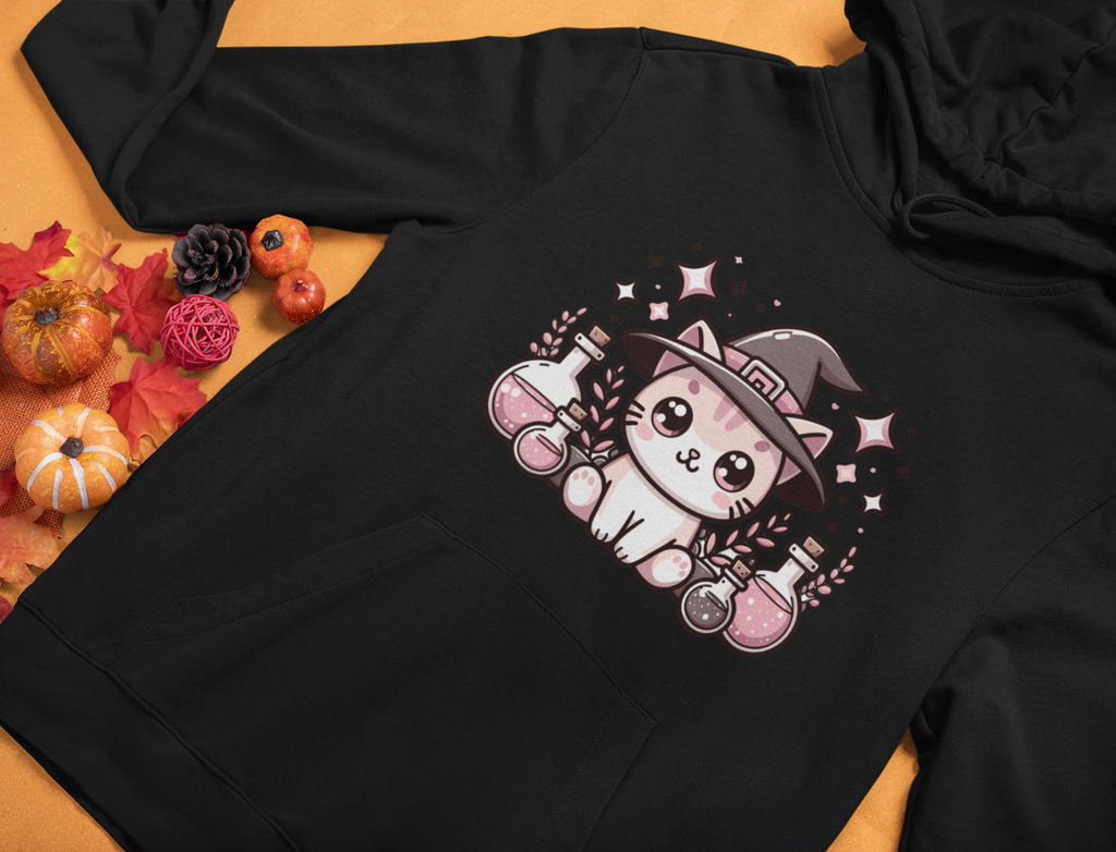 Black hoodie with a cute cat in a witch hat design on a wooden surface with fall decorations.